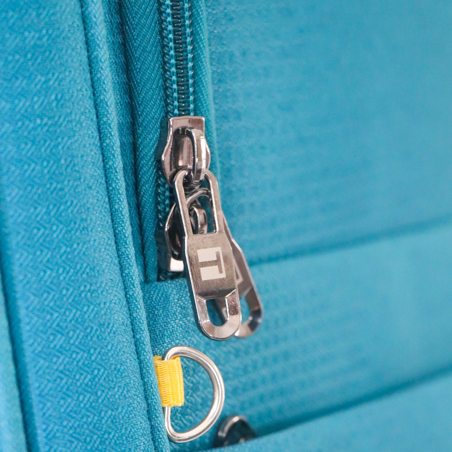 Close-up of the premium zipper on blue Salsa Plus luggage featuring a metallic puller engraved with the Timus ‘T’ logo for a branded touch.