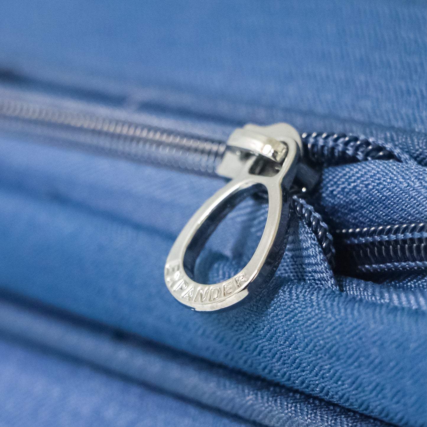 Close-up of the expandable zipper on navy blue Salsa Plus luggage, designed to increase packing space with a smooth-running zip mechanism.