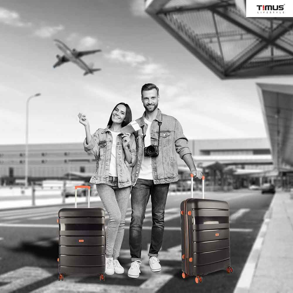 A man and woman standing at the airport holding Sunlite orange black hard trolley bags, showcasing a travel-ready lifestyle with stylish luggage.