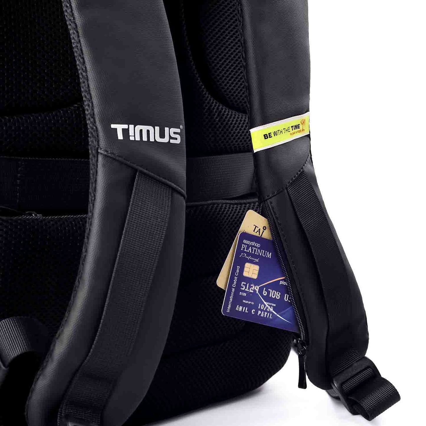 Close-up view of the Timus Madrid Backpack's shoulder straps showing a hidden zippered pocket holding a credit card and tag, with "BE WITH THE TIME" branding detail.