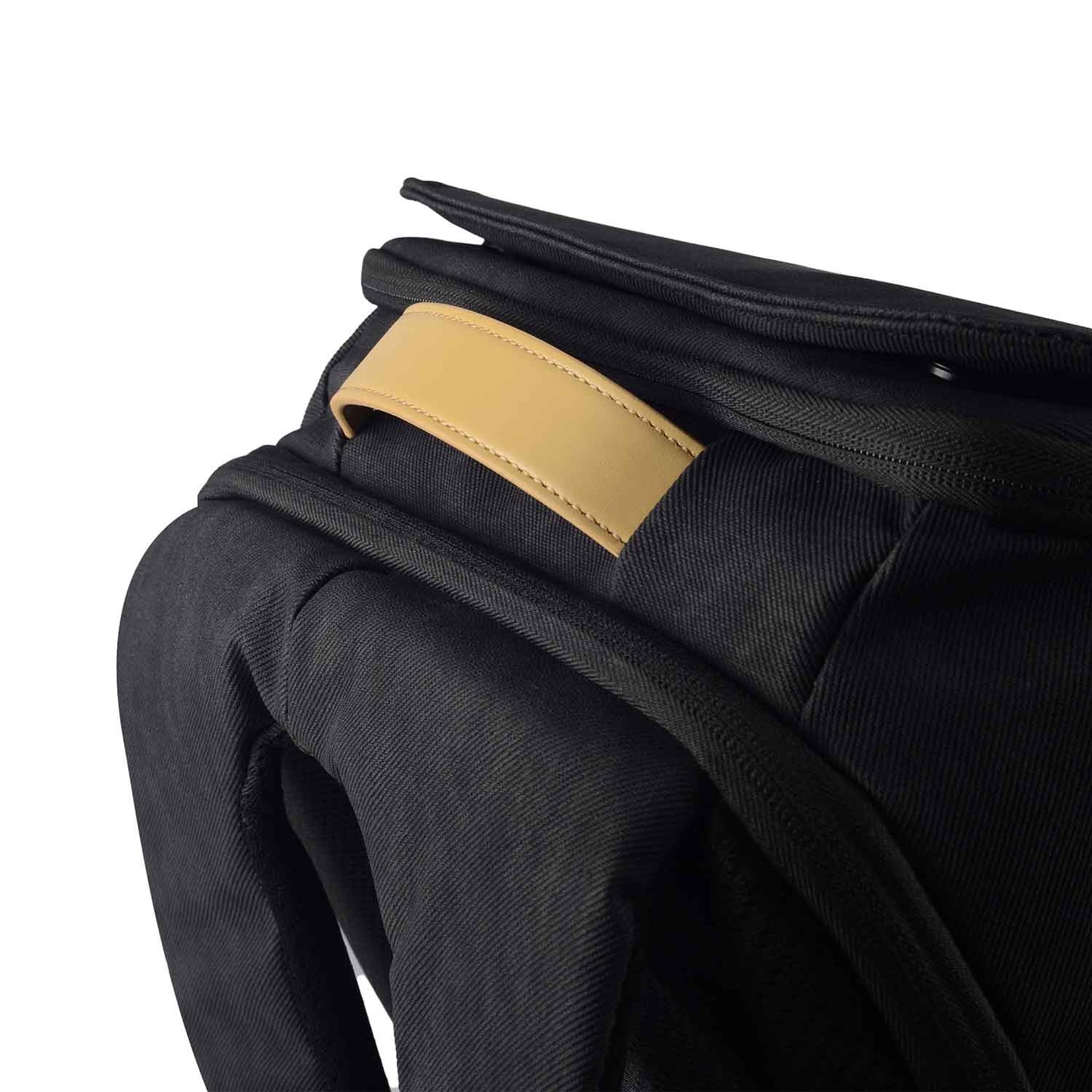 Close-up of the black Timus Magnet Overnighter backpack showing the tan leather handle on the top, with padded shoulder straps visible beneath.