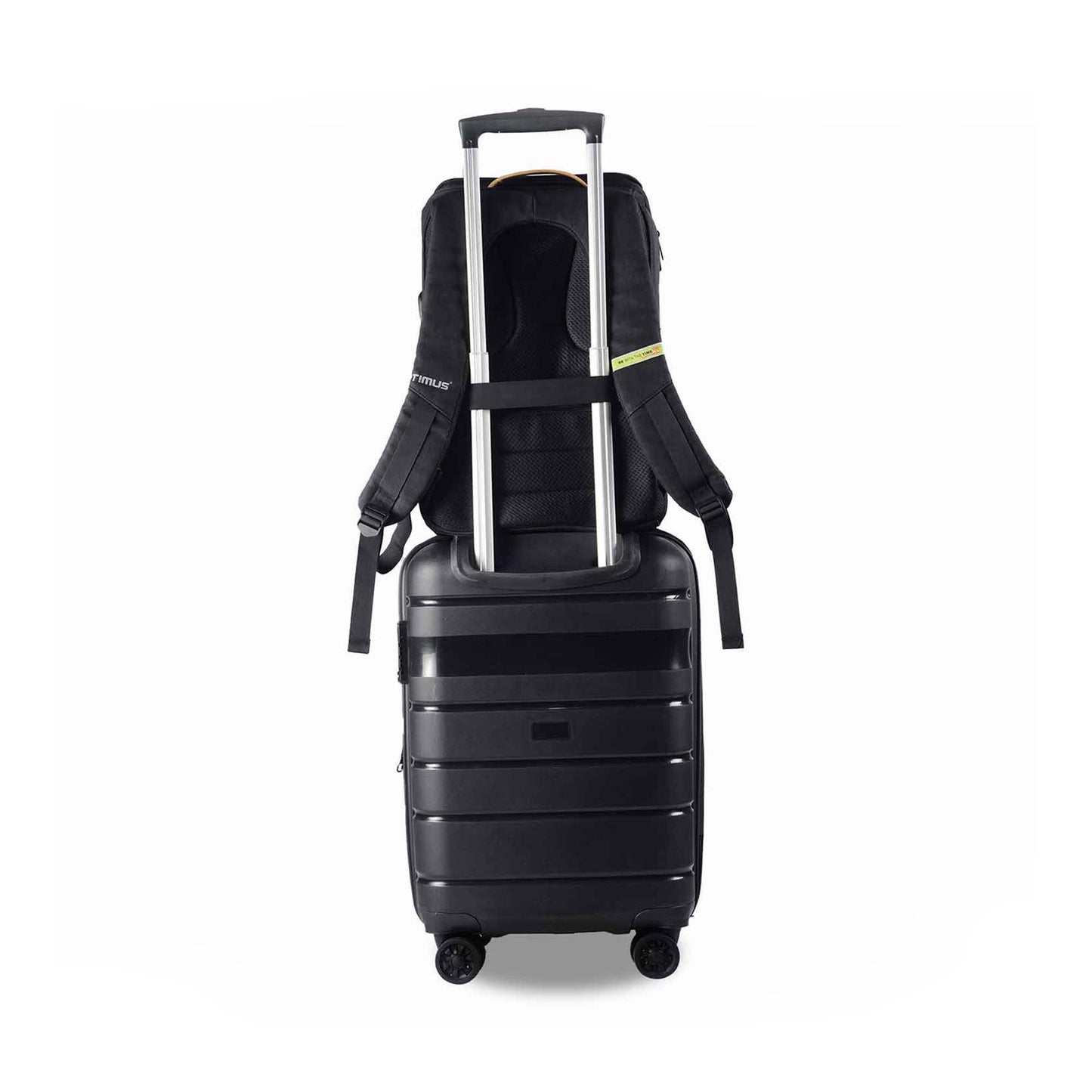 Back view of the Timus Magnet Overnighter backpack attached securely to the handle of a black rolling suitcase using its luggage strap. The suitcase has four wheels and is placed against a white background.
