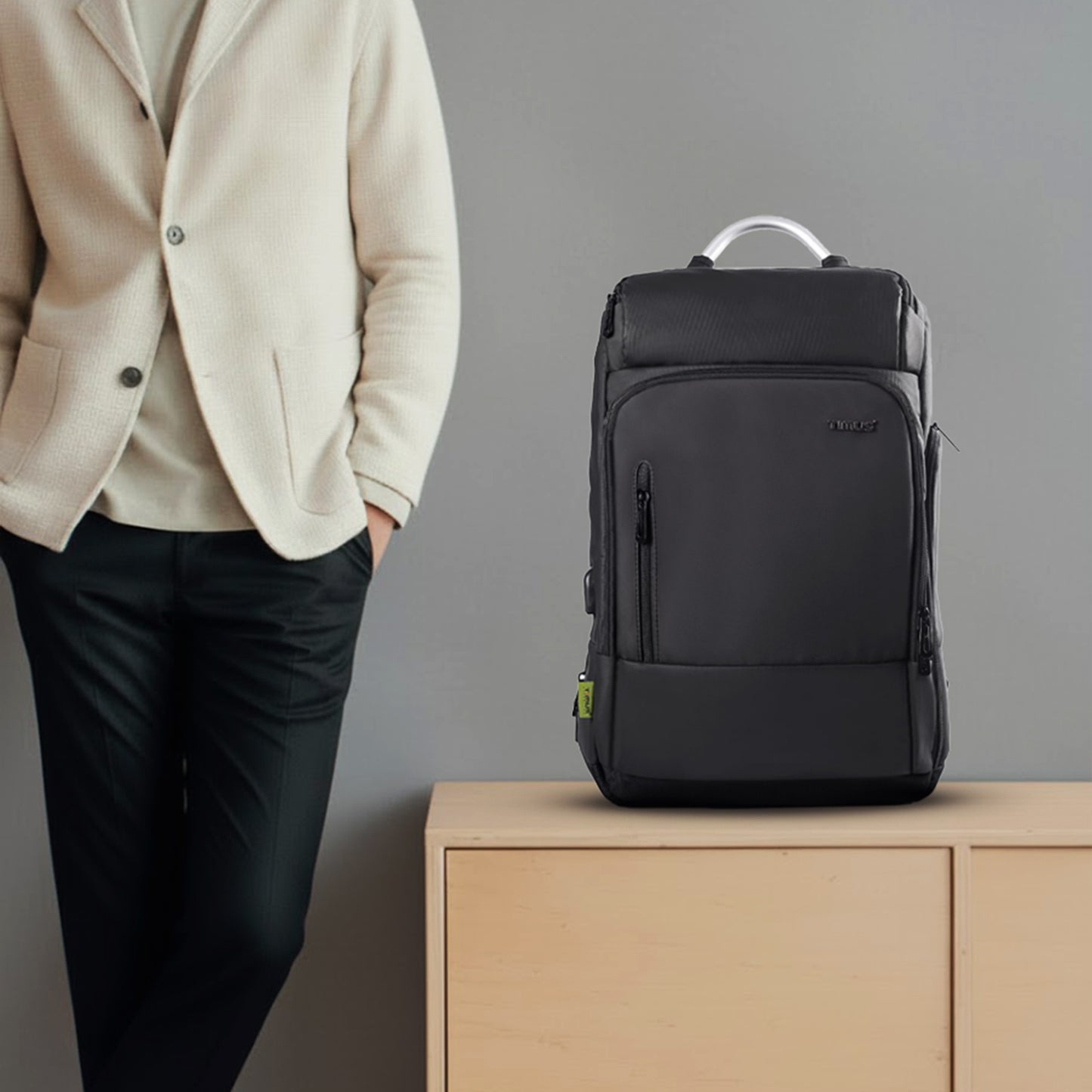 Black backpack on a wooden surface with a person wearing a beige jacket in the background