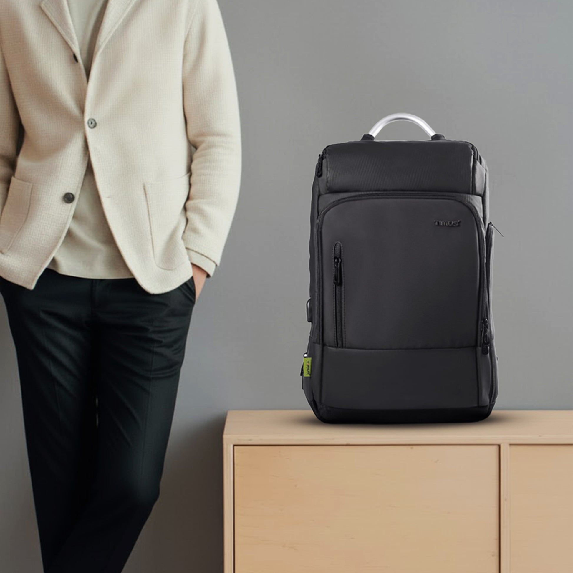 Black backpack on a wooden surface with a person wearing a beige jacket in the background