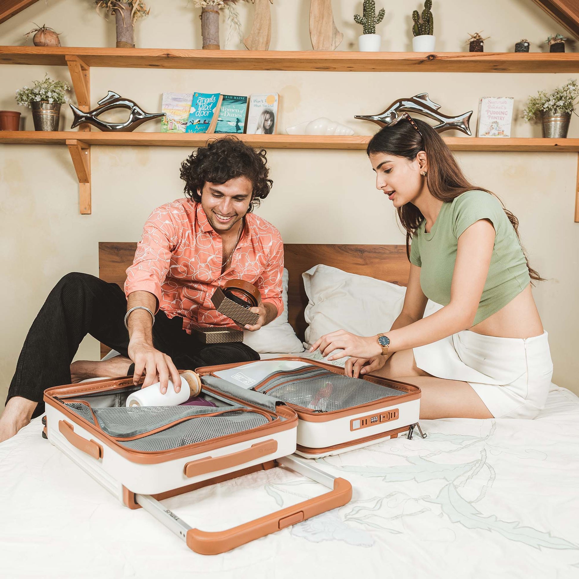 Young couple packing a Timus Starlite ivory trolley bag on a bed, highlighting spacious organized interior and stylish design.
