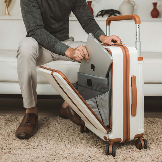 Man placing a laptop into the front compartment of Timus Starlite ivory colour hard trolley, featuring a padded organizer sleeve, smooth dual spinner wheels, and tan leather-textured accents.
