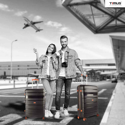  A man and woman standing at the airport holding Sunlite orange black hard trolley bags, showcasing a travel-ready lifestyle with stylish luggage.