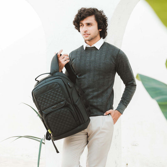 Man in smart casual outfit holding Berlin black professional backpack with quilted front, photographed in bright outdoor setting.