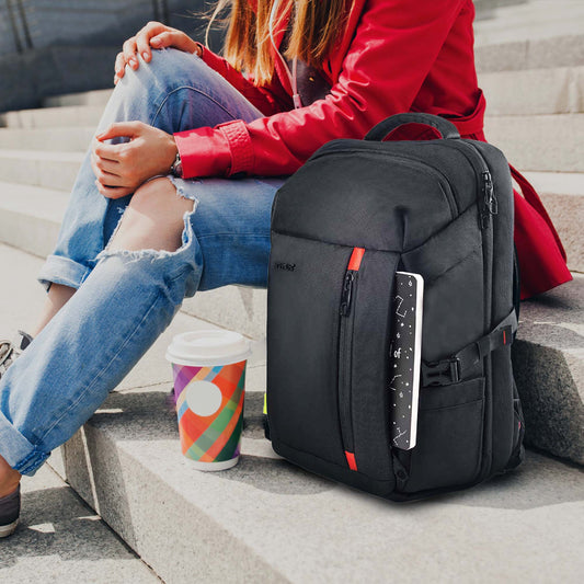 Black London laptop backpack with red accents resting on concrete steps beside a colorful takeaway coffee cup, with a woman wearing ripped blue jeans and a red jacket sitting nearby.