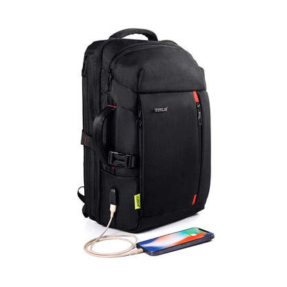 right front angled view of black London laptop backpack by TIMUS showing padded handle, USB charging port with cable connected to a smartphone, multiple zippered compartments, side handle for easy carrying, and red accent details.