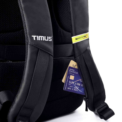 Close-up view of the Timus Madrid Backpack's shoulder straps showing a hidden zippered pocket holding a credit card and tag, with "BE WITH THE TIME" branding detail.