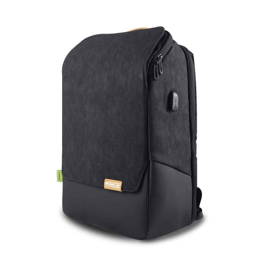 Left front angled view of black Timus Magnet Overnighter professional backpack showing textured fabric flap with leather-like bottom, small Timus logo patch, USB charging port on the side, and green Timus tag on a white background.