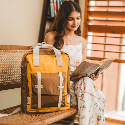 Timus Miami yellow urban backpack on a bench with a woman reading indoors.