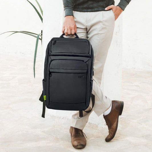 Man wearing a grey sweater and beige pants holding a sleek black Tokyo laptop backpack by its top handle, showcasing its minimalist design and multiple front compartments.
